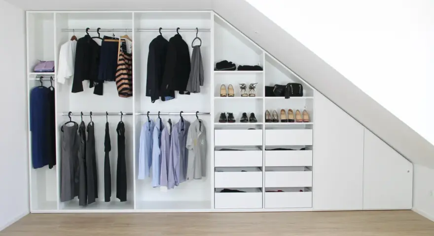 Einbauschrank selber bauen: Weißer Schrank mit Kleiderstangen, Schubladen und Schuhfächern unter einer Dachschräge.