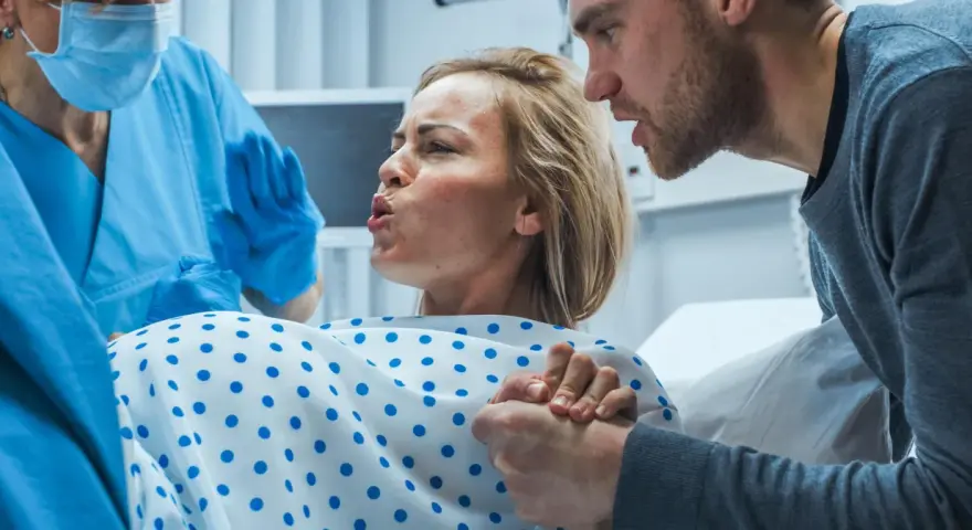 Kobieta rodzi, wspierana przez partnera i położną. W tej chwili kluczowa jest oksytocyna, hormon miłości i porodu.