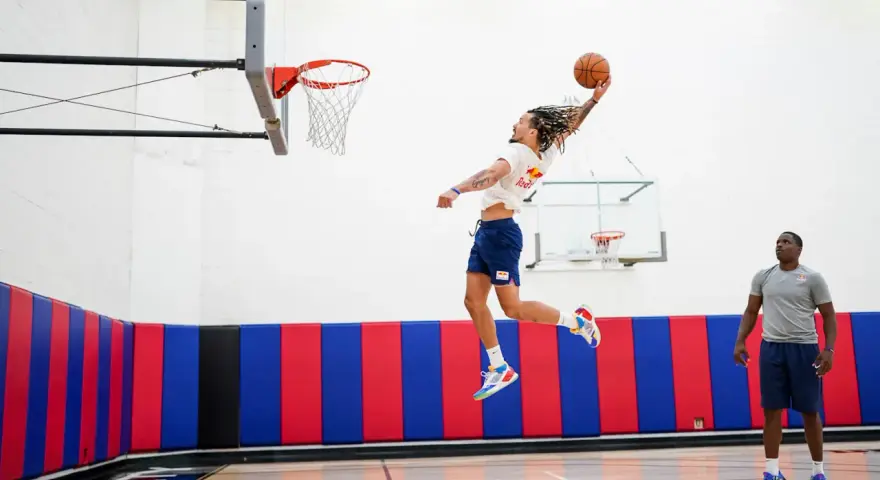 Un joueur de basket-ball en plein saut, ballon en main, effectue un exercice de pliométrie. Un autre joueur observe.
