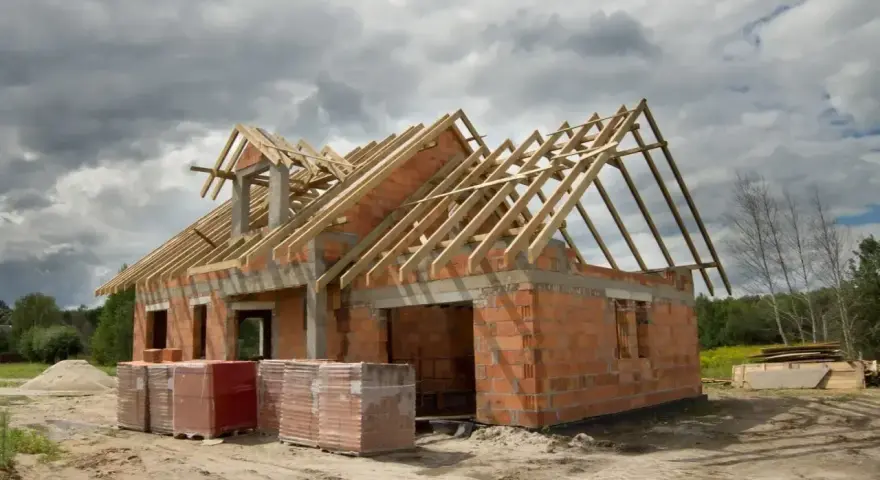 Budowa domu 220m2 w stanie surowym. Ceglane ściany, drewniany dach, materiały budowlane na placu.
