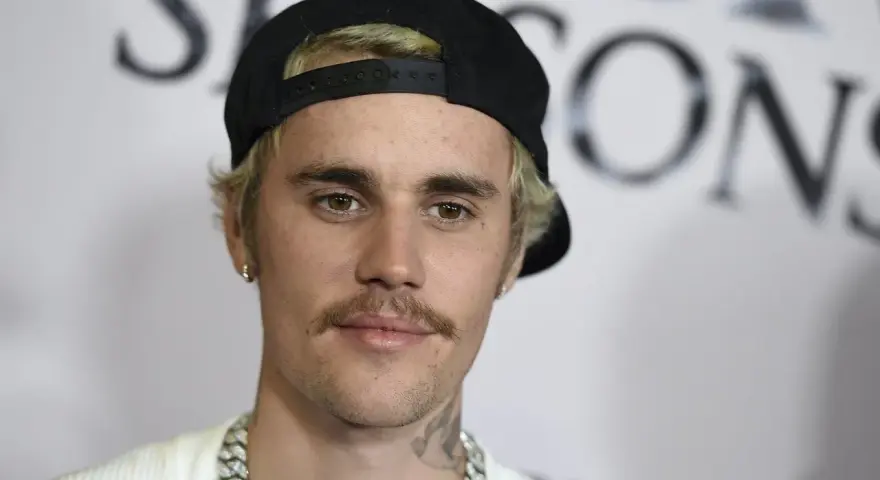 Justin Bieber con un gorra negra y un bigote herradura, luciendo una cadena plateada.