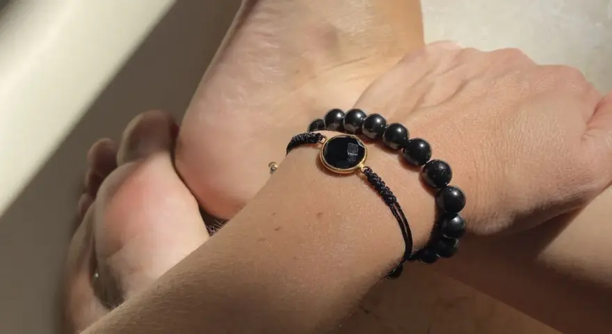 Pulsera con cuentas de obsidiana, una piedra negra protectora, junto a unos pies.