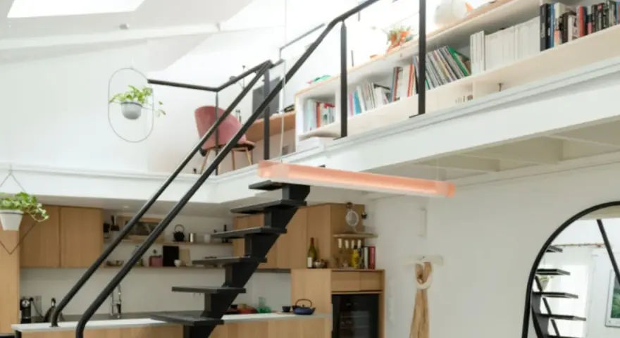 Aménagement mezzanine ouverte avec escalier métallique, cuisine en bois, étagères remplies de livres et plantes suspendues.