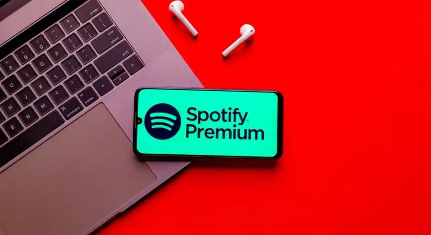 Laptop, telefon ze Spotify Premium i słuchawki na czerwonym tle.