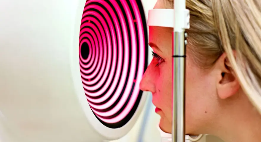 Esame oculistico: una donna guarda un dispositivo che proietta una mappa corneale a spirale rosa e nera.