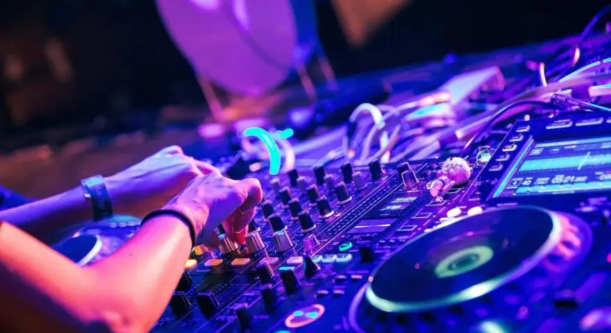 Hände am DJ-Pult, die die Regler für verschiedene techno genres bedienen. Neonlicht und pulsierende Beats.