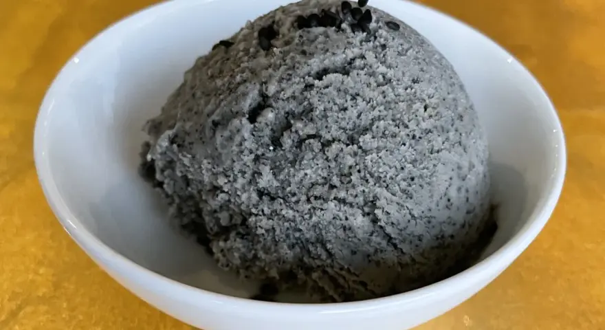Ein Löffel cremiges Sesam Eis, garniert mit schwarzen Sesamkörnern, in einer weißen Schale.