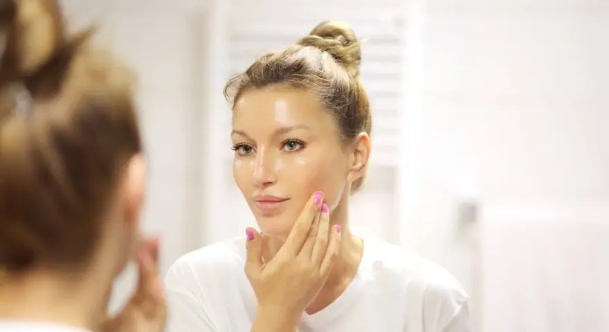 Donna con capelli raccolti applica un siero sul viso. La domanda è: quanti sieri si possono usare insieme per una pelle luminosa?