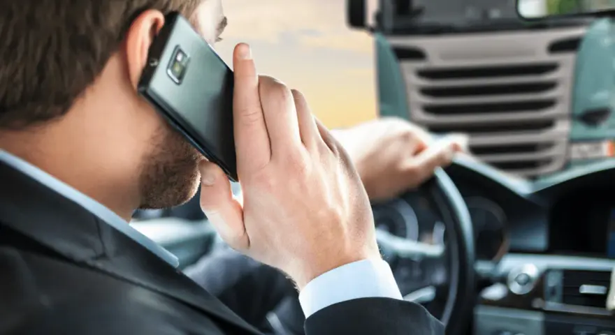 Biznesmen w garniturze rozmawia przez telefon, siedząc za kierownicą ciężarówki. To symbol odpowiedzialności spedytora.