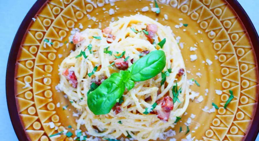 Pyszna carbonara ze szparagami, udekorowana bazylią i posypana parmezanem, na ozdobnym talerzu.