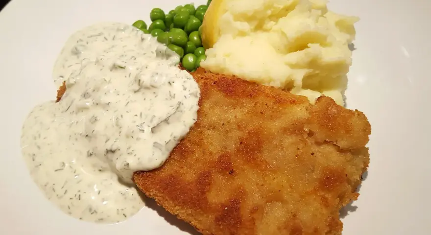 En gyllene panerad fisk med krämig sås, ärtor och potatismos. En klassisk och god måltid.
