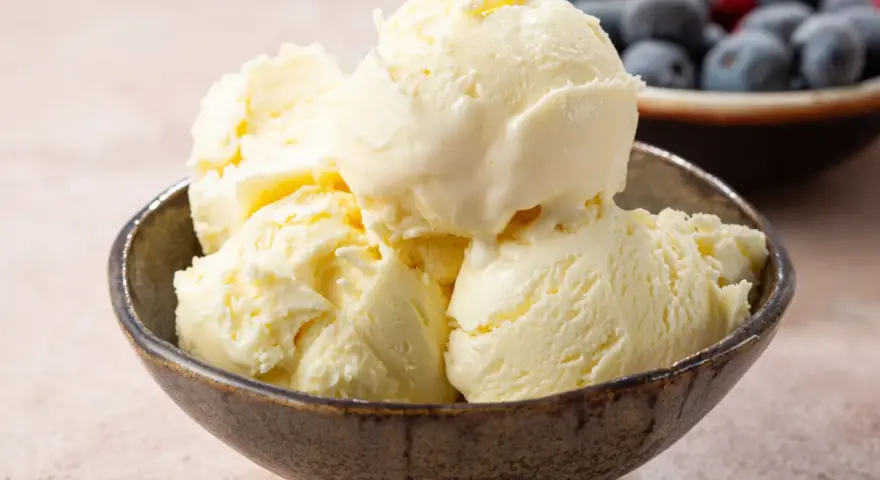Pyszne, kremowe lody waniliowe w miseczce. Idealne na deser, gdy szukasz prostego przepisu na lody. W tle miska z jagodami i malinami.