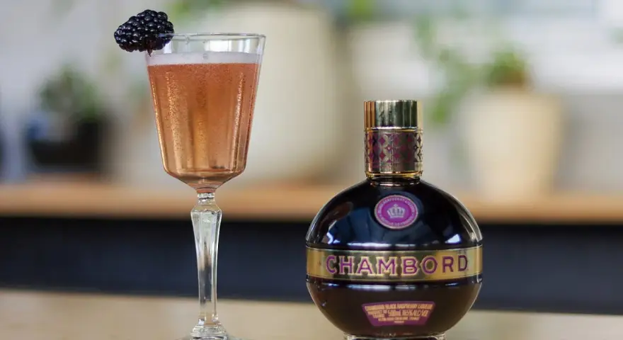 Chambord likier jak pić? Elegancki kieliszek z różowym drinkiem i jeżyną obok butelki likieru. Idealny na specjalne okazje.
