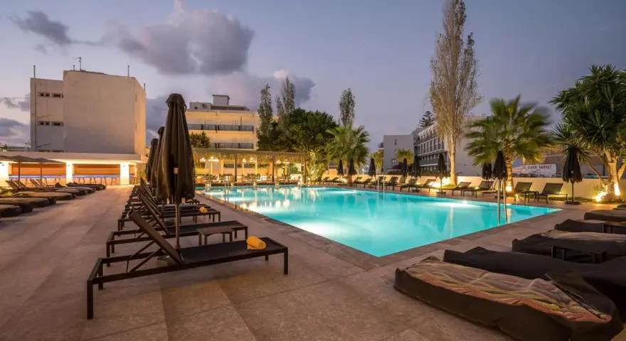 Basen hotelowy oświetlony nocą, leżaki i palmy. Idealne miejsce na relaks, zgodnie z licznymi heronissos hotel opinie.