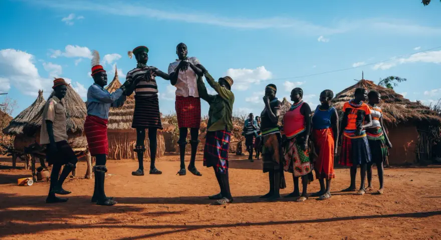 Ludzie w tradycyjnych strojach tańczą przed chatami. Czy Uganda jest bezpiecznie? Tak, w takich miejscach można poczuć się bezpiecznie.