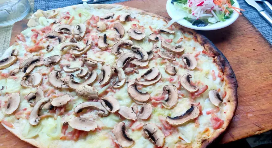 Tarta flambeada con champiñones y bacon, servida sobre tabla de madera. Una pequeña ensalada acompaña.