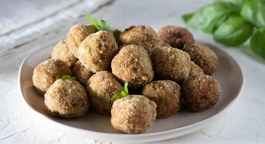 Un piatto pieno di polpette di melanzane dorate e croccanti, guarnite con prezzemolo fresco.