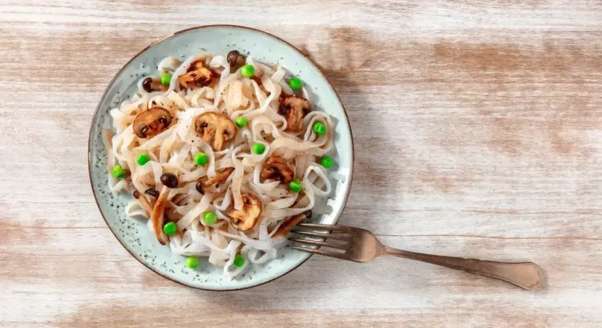 Makaron konjac jak smakuje? Delikatny, z grzybami i groszkiem, na talerzu.
