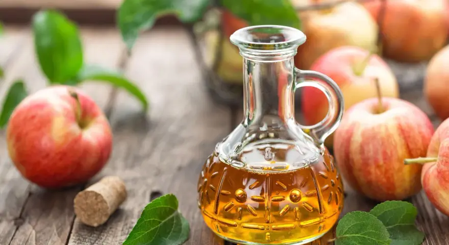 Aceto di mele in un decanter, mele rosse e foglie verdi su un tavolo di legno. Un rimedio naturale per sapere come eliminare i funghi della pelle velocemente.