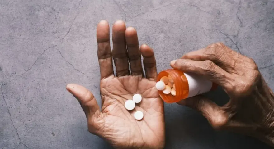 Dłoń wysypuje tabletki Tylenol z pomarańczowej buteleczki.