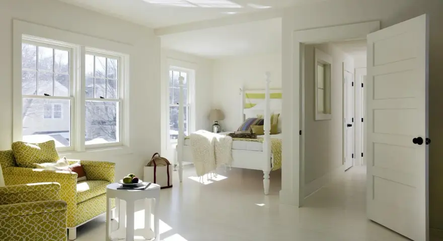 Luminosa camera da letto con **colore pareti bianco caldo**, due poltrone gialle, letto a baldacchino e luce solare che filtra dalle finestre.