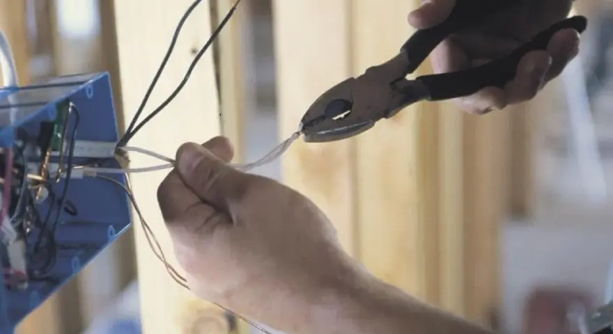 Ręce przycinają przewody do skrzynki elektrycznej. To kluczowy krok, by dowiedzieć się, jak zostać elektrykiem.