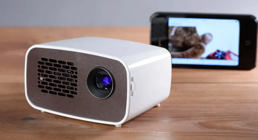 Kleiner Beamer mit Handy verbinden für Heimkino. Ein Smartphone zeigt ein Bild, während der Beamer bereit ist.