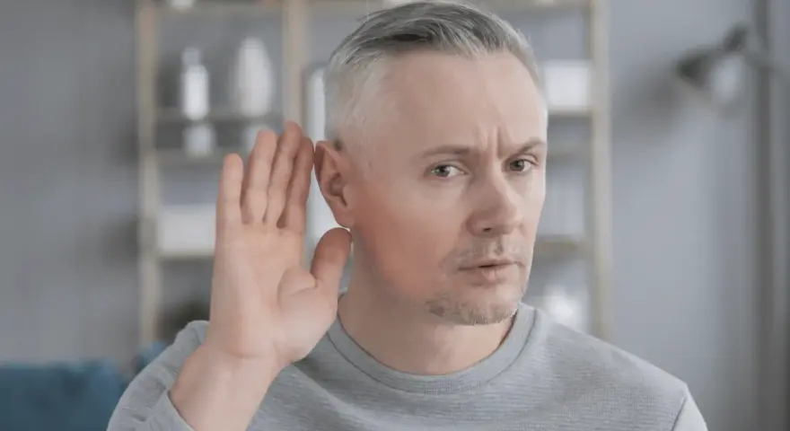 Mężczyzna z siwymi włosami przykłada dłoń do ucha, próbując usłyszeć. Czy to początek zawalu ucha?