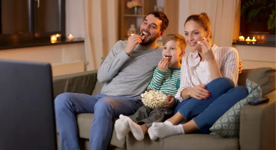 Rodzina zajada popcorn podczas oglądania filmów familijnych.