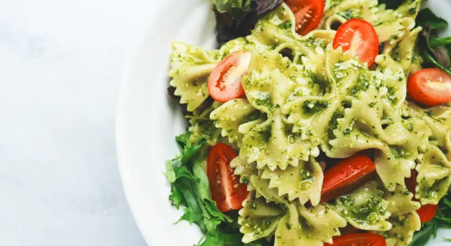 Ein köstlicher Nudelsalat mit Pesto, garniert mit frischen Kirschtomaten und Salatblättern.