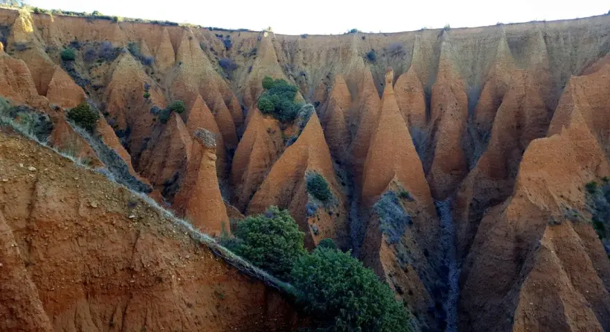 Paisaje erosionado con formaciones cónicas de tierra rojiza, vegetación escasa y un camino que parece el pontón de la oliva ruta circular.