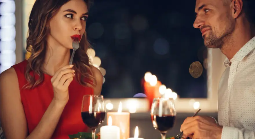 Romantyczna kolacja przy świecach. Ona, w czerwonej sukience, zmysłowo je, a on patrzy na nią z uwielbieniem. Widać oznaki flirtu dziewczyny w jej spojrzeniu.