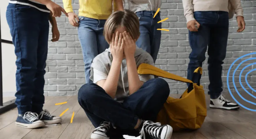 Dziecko zakrywa twarz, otoczone przez inne dzieci, które wskazują palcami. To obraz tego, czym jest bullying.