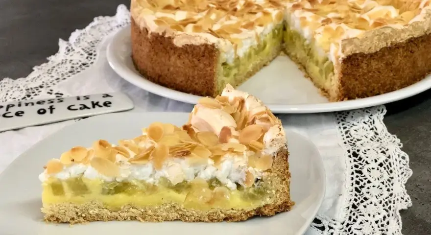 Ein köstlicher Rhabarberkuchen mit Pudding und Baiser, bestreut mit Mandelblättchen. Ein Stück Glück auf einem Teller.