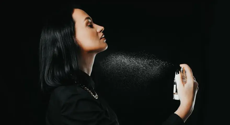 Kobieta rozpyla perfumy na szyję na czarnym tle.
