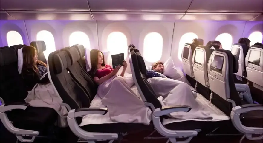 Komfortowy **business class lot**. Pasażerowie odpoczywają, czytają i śpią w wygodnych fotelach, otuleni kocami.