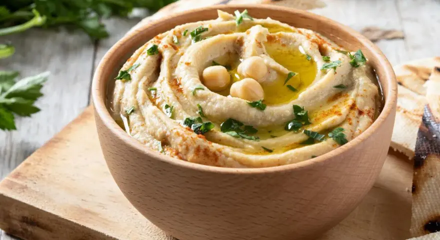 Hummus cremoso en cuenco de madera, decorado con garbanzos, aceite de oliva, perejil y pimentón.