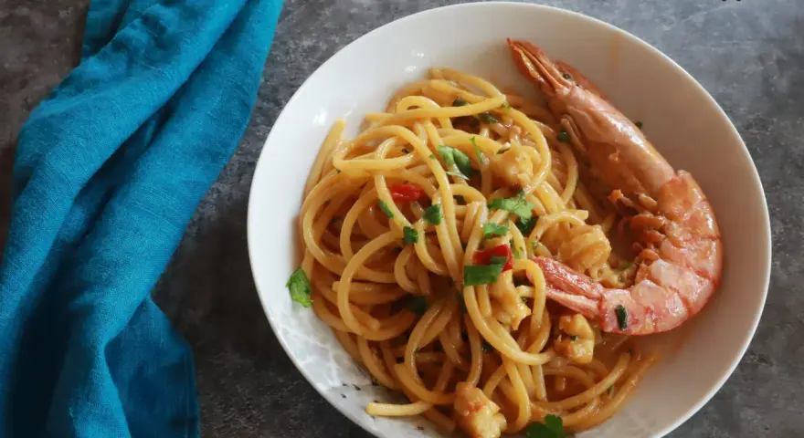 Spaghetti con gamberoni surgelati, un piatto gustoso e veloce. Un gamberone intero adorna la pasta condita con pomodorini e prezzemolo.