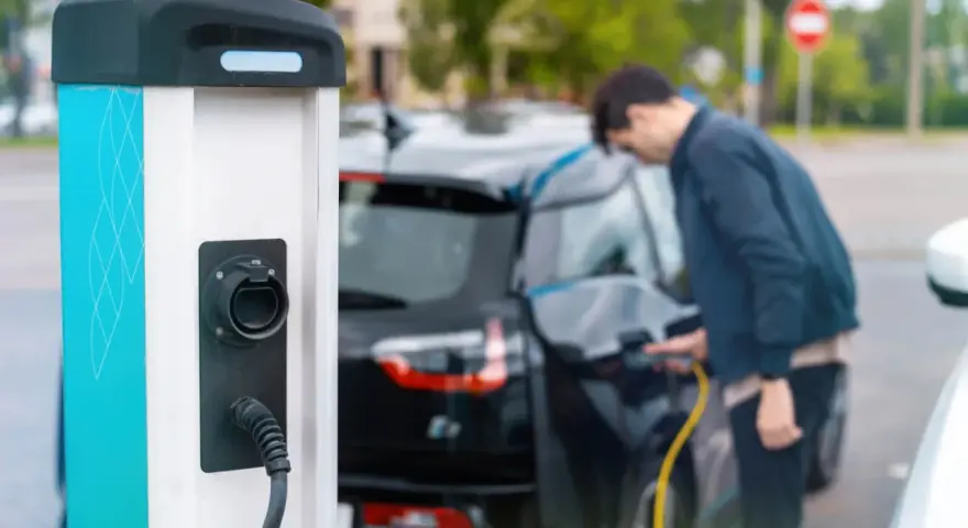 Mój elektryk czeka na ładowanie. Mężczyzna podłącza kabel do samochodu przy stacji ładowania.