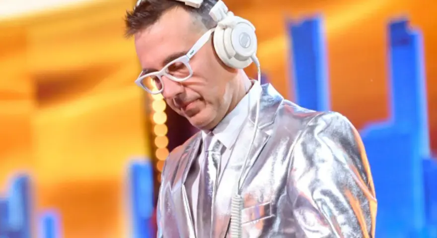 DJ w błyszczącej marynarce i białych okularach, słuchawki na uszach, gotowy do zagrania "Jaka to melodia".
