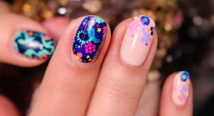 Comment avoir de beaux ongles : des ongles décorés de motifs floraux colorés et de petites étoiles sur fond bleu nuit ou nude.