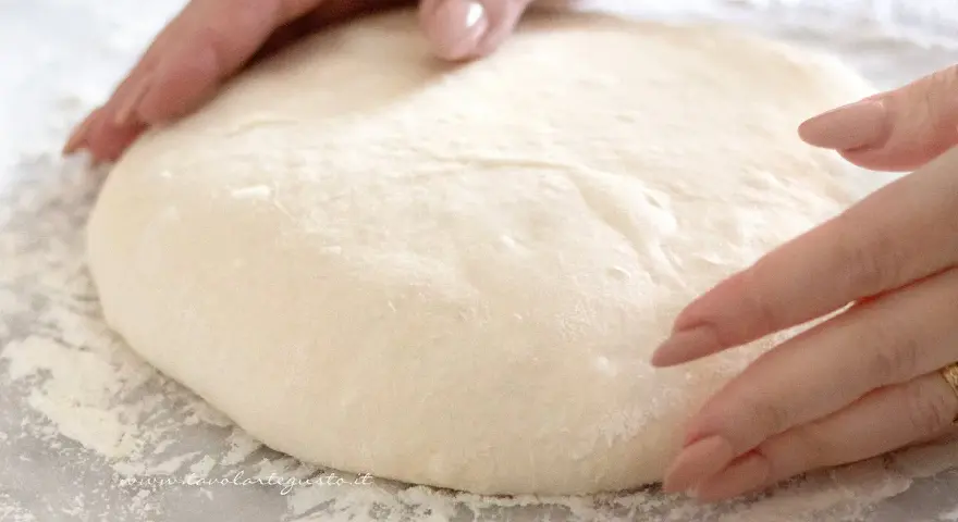 Mani che lavorano un impasto pizza veloce, soffice e pronto per essere steso.