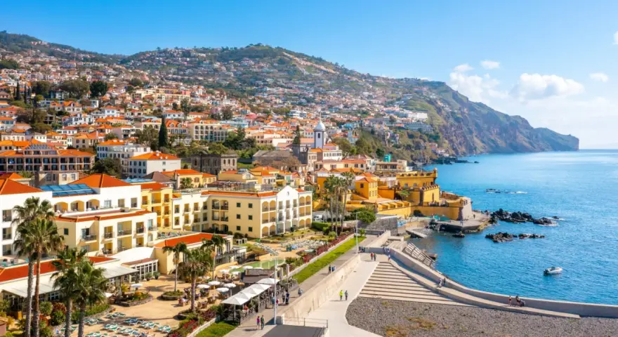 Widok na Funchal, stolicę Madery, z kolorowymi budynkami wznoszącymi się na zboczu góry, otoczonymi błękitnym oceanem.