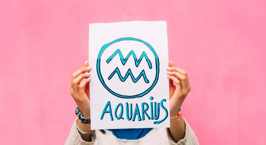 Waga i Wodnik: przyjaźń w kolorach tęczy. Ręce trzymają plakat z symbolem Wodnika i napisem "Aquarius" na różowym tle.