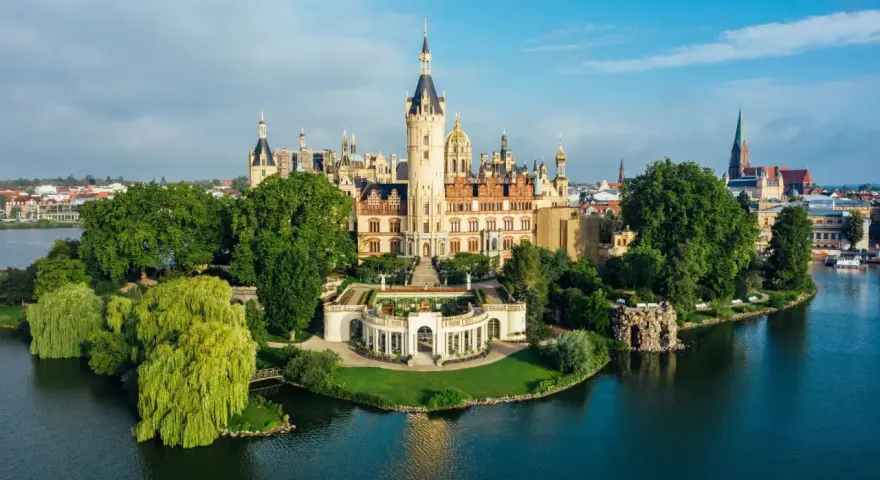 Schweriner Schloss auf einer Insel, umgeben von Wasser und grünen Bäumen. Ein Märchenschloss, das zu den Schwerin Geheimtipps zählt.