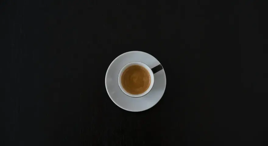 Czarna filiżanka espresso na białym spodeczku na ciemnym tle. Może symbolizować początek walki z objawami odstawienia kofeiny.
