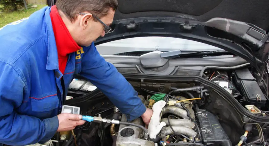 Mechanik w niebieskim kombinezonie sprawdza silnik diesla, używając przyrządu.