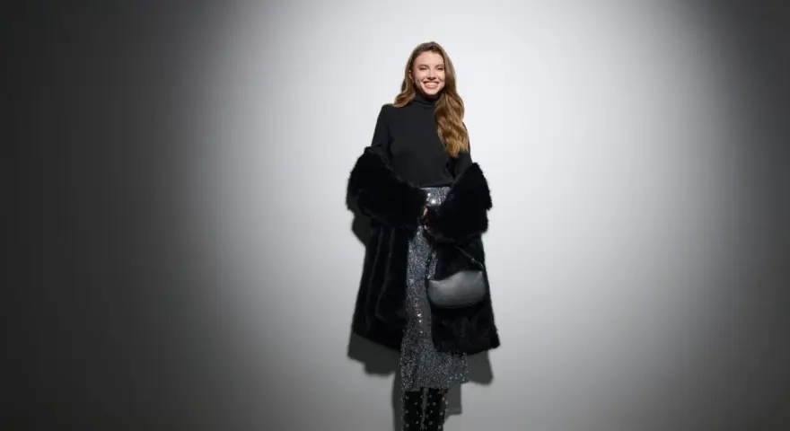 Uśmiechnięta kobieta w błyszczącej spódnicy i futrzanym płaszczu. Czy do filharmonii trzeba ubrać się elegancko? Ta stylizacja sugeruje, że tak!
