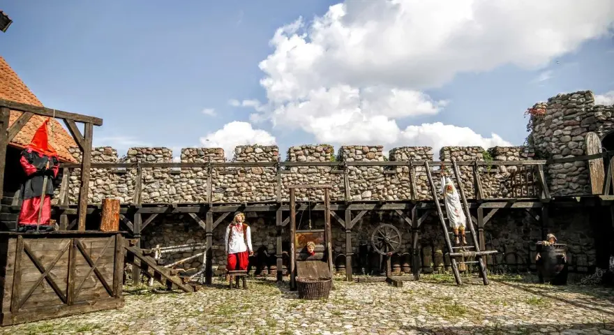 Scena z Muzeum Tortur w Krakowie: gilotyna, postacie w strojach historycznych i kamienne mury.