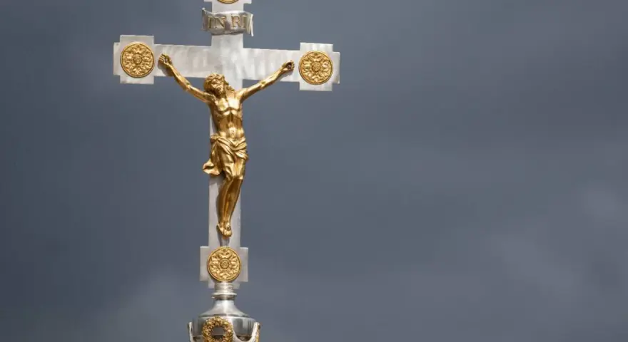 Ein goldenes Kruzifix mit Jesus vor dramatischem Himmel. Die Frage, wie lange dauert die Osterzeit, hallt nach.